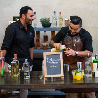Expert mixologists preparing craft cocktails with Mexican spirits and fresh ingredients at a bar station.