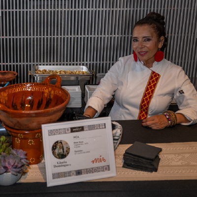 Portrait of a female chef in a traditional white jacket featuring Mexican embroidery at her culinary station.